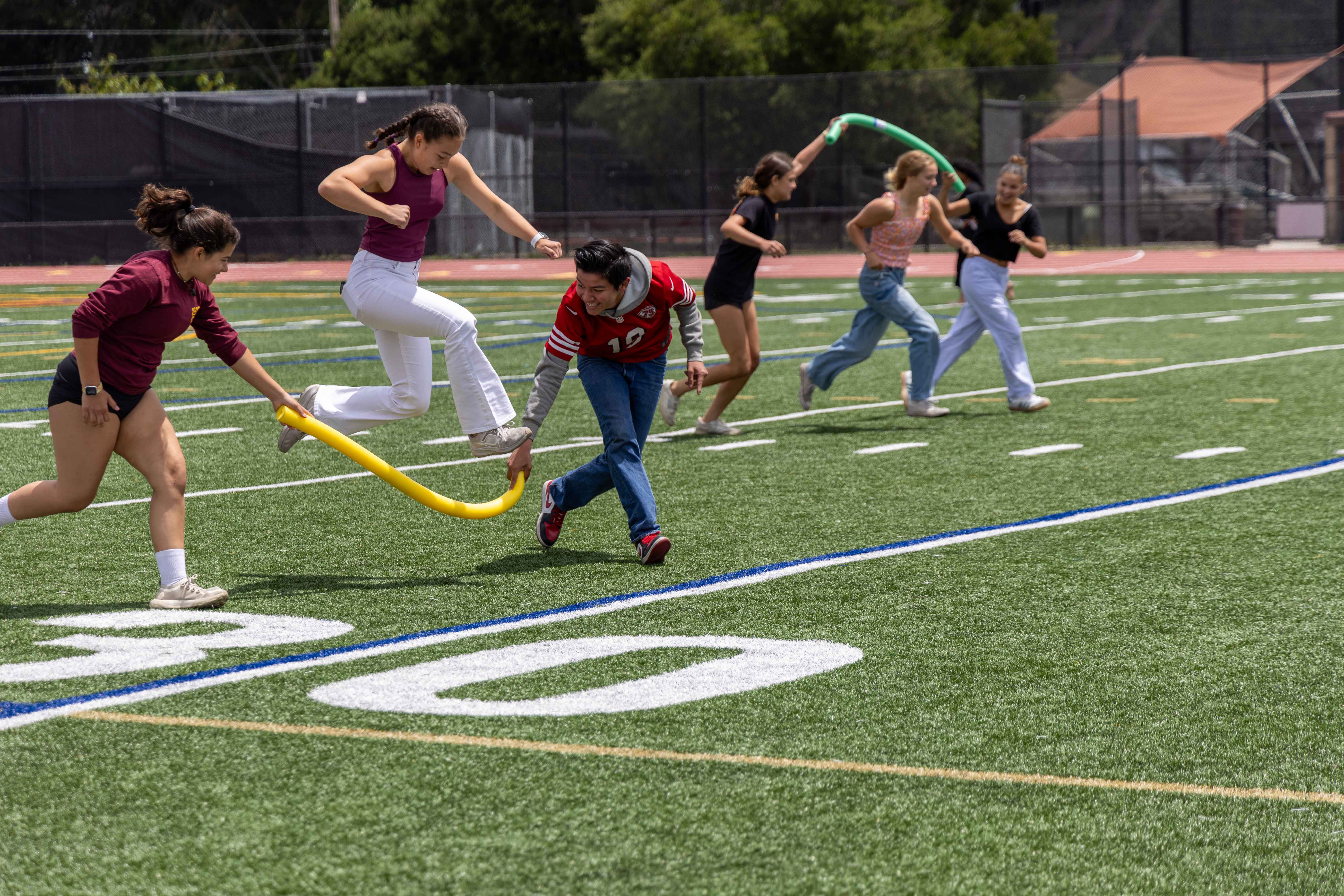 Students race in a jump rope activity with pool noodles.