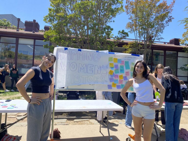 Juniors Aliyah Chowdhary-Fitton (left) and Antonia Mille (right) pose in front of their display for their Feminists: Reformers Throughout History club.