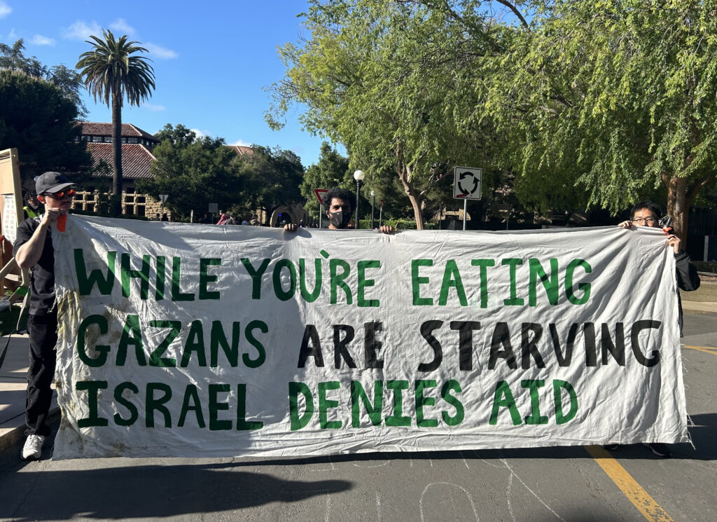 Protest sign at Stanford University that reads "While you're eating, Gazans are Starving. Israel denies aid.